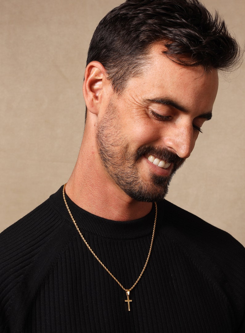 May include: A man wearing a black sweater with a gold rope chain necklace and a small gold cross pendant.
