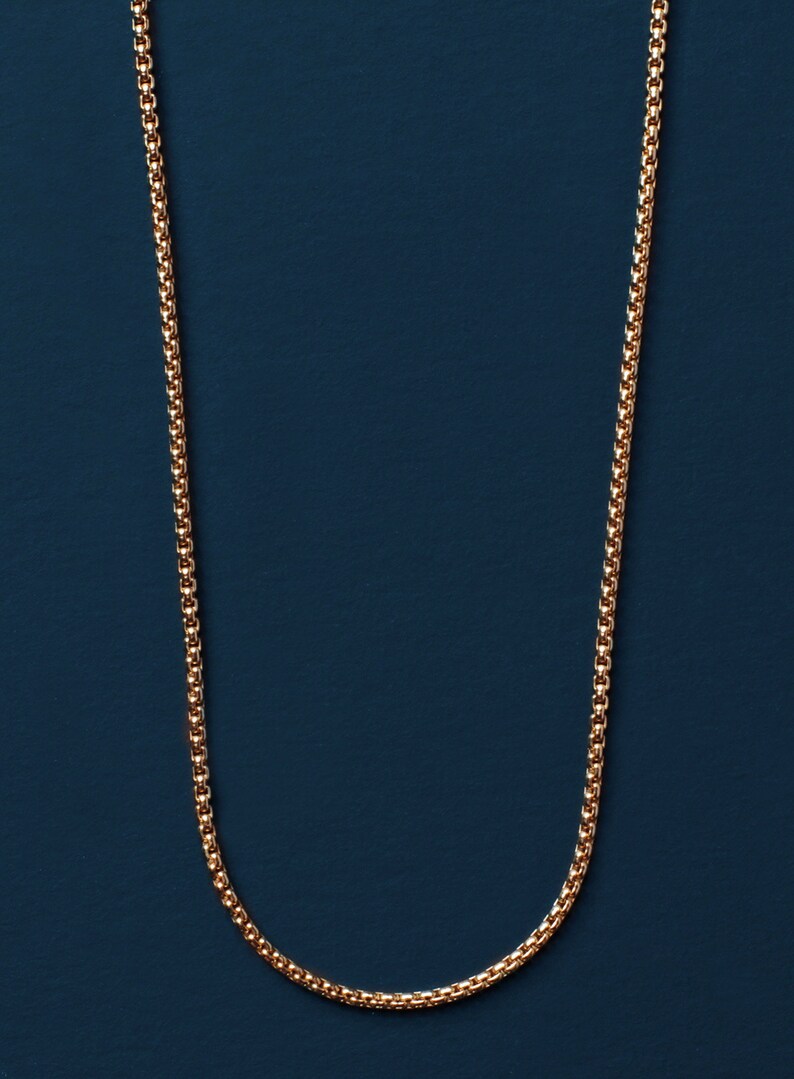 Puede incluir: Un collar de cadena de oro sobre un fondo azul oscuro.