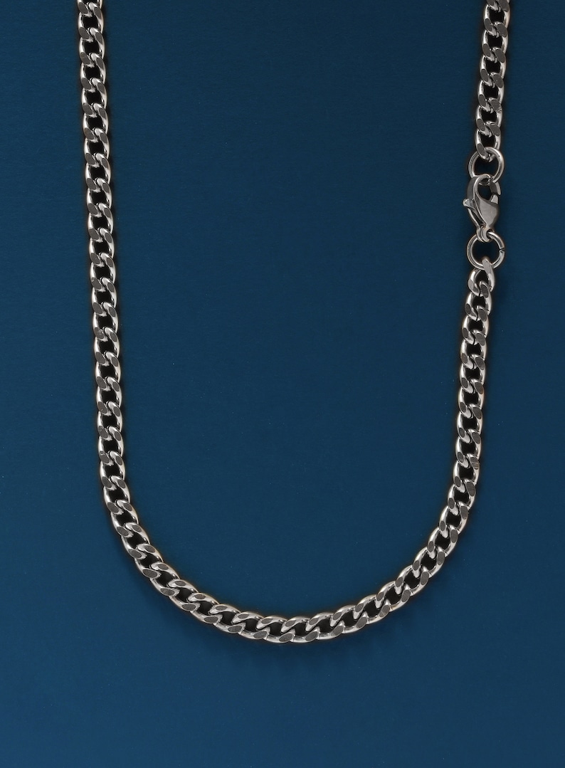 May include: A silver chain necklace with a lobster clasp closure. The chain is on a blue background.