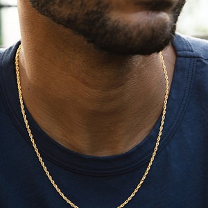 May include: A gold rope chain necklace on a person's neck. The chain is thin and delicate.