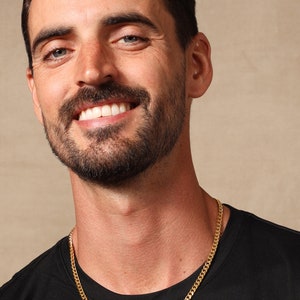 May include: A gold chain necklace on a person wearing a black t-shirt.