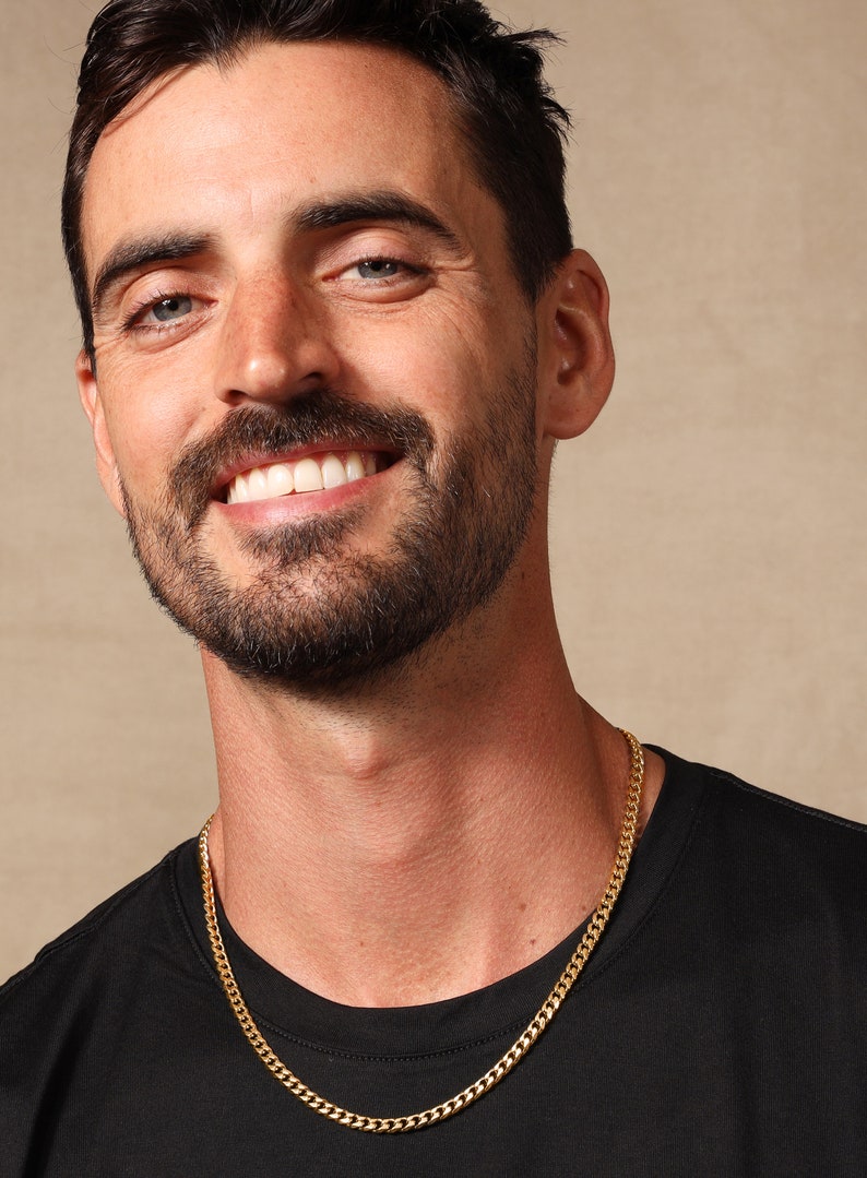 May include: A gold chain necklace on a person wearing a black t-shirt.