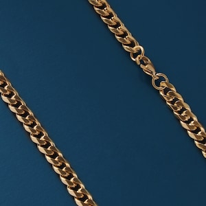 May include: A gold chain necklace with a curb link style. The chain is on a blue background.
