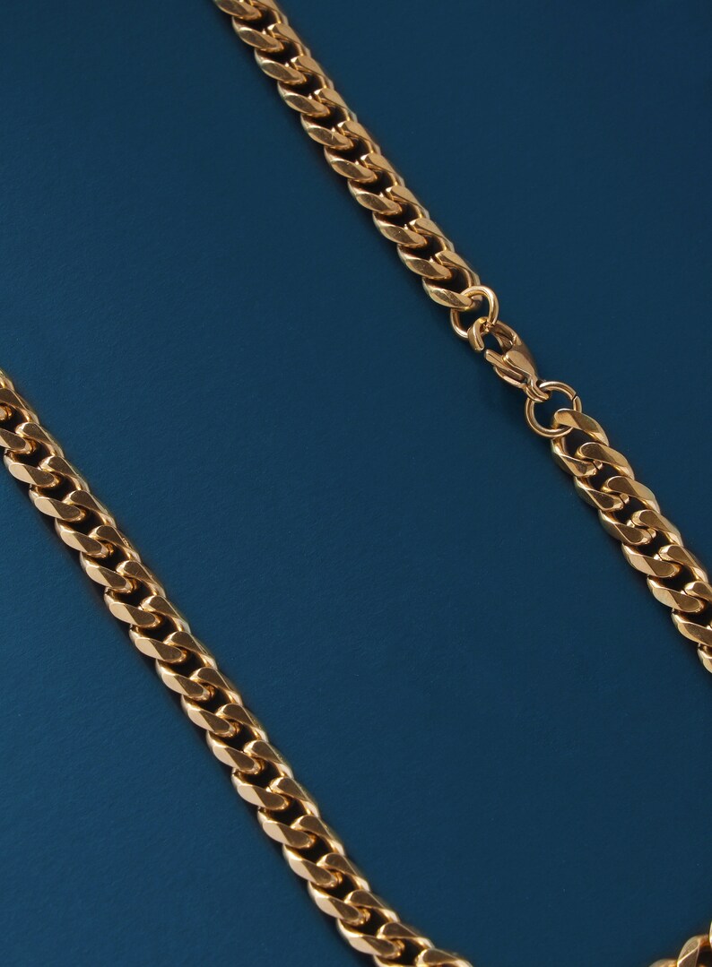 May include: A gold chain necklace with a curb link style. The chain is on a blue background.