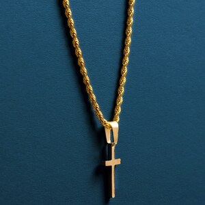 May include: A gold chain necklace with a small gold cross pendant. The necklace is on a blue background.