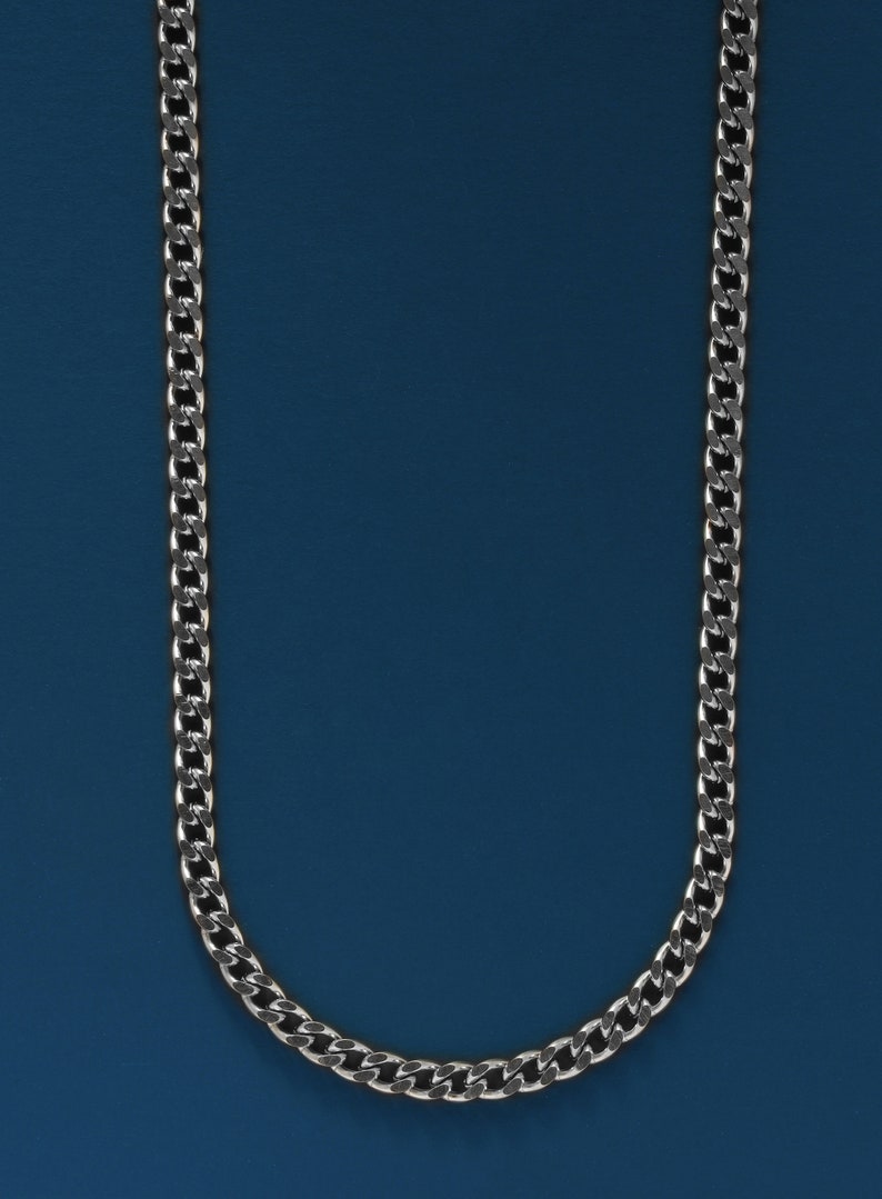 May include: A silver chain necklace against a blue background.