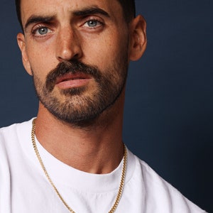 May include: A man wearing a white t-shirt with a gold chain necklace.