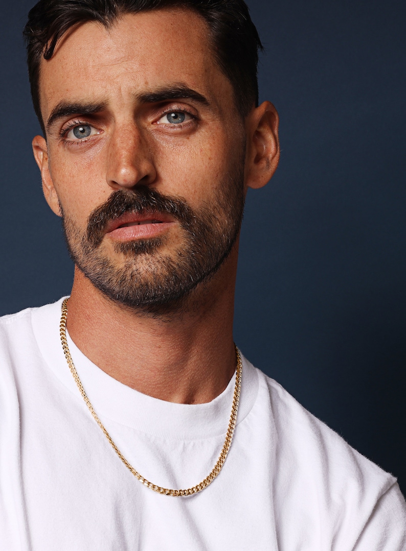 May include: A man wearing a white t-shirt with a gold chain necklace.