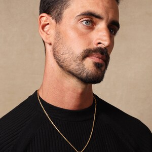May include: A man wearing a black sweater with a gold rope chain necklace and a small gold cross pendant.