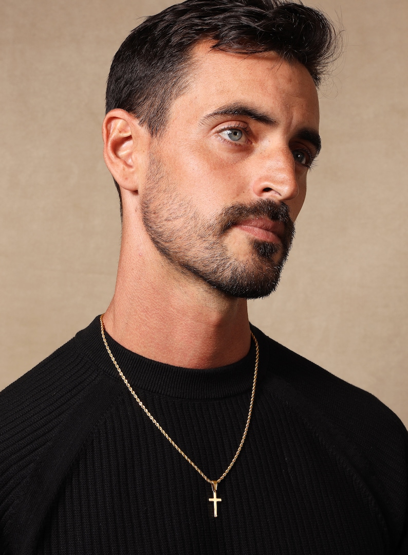 May include: A man wearing a black sweater with a gold rope chain necklace and a small gold cross pendant.
