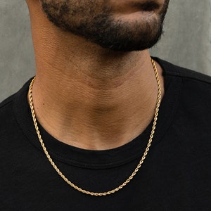 May include: A gold rope chain necklace on a person wearing a black shirt.