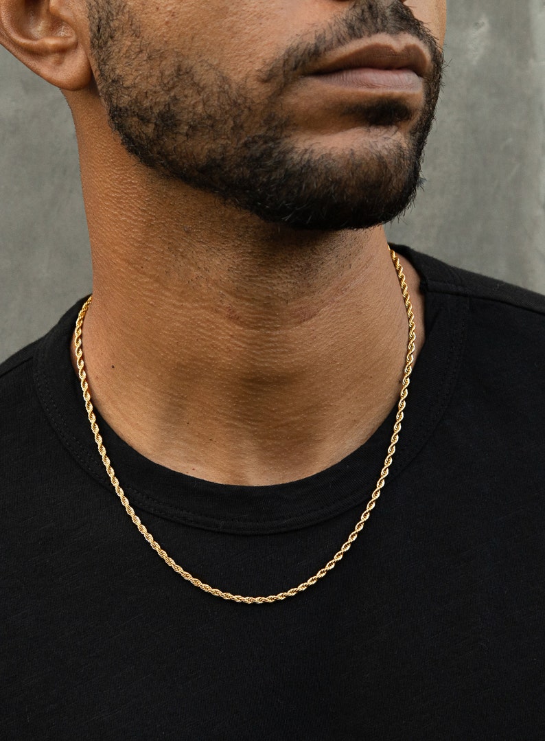 May include: A gold rope chain necklace on a person wearing a black shirt.