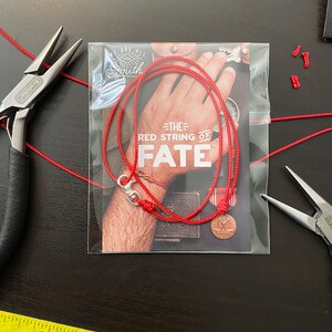 May include: Red string bracelet with a silver clasp and a small round charm. The bracelet is packaged in a clear plastic bag with a card that reads "The Red String of Fate".