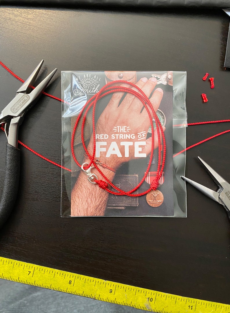 May include: Red string bracelet with a silver clasp and a small round charm. The bracelet is packaged in a clear plastic bag with a card that reads "The Red String of Fate".