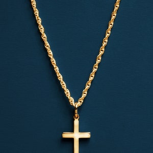 May include: A gold chain necklace with a simple gold cross pendant against a dark blue background.