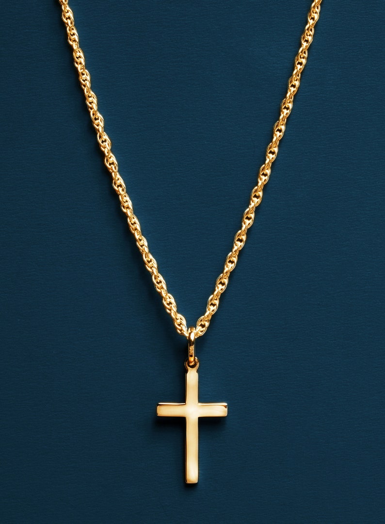 May include: A gold chain necklace with a simple gold cross pendant against a dark blue background.