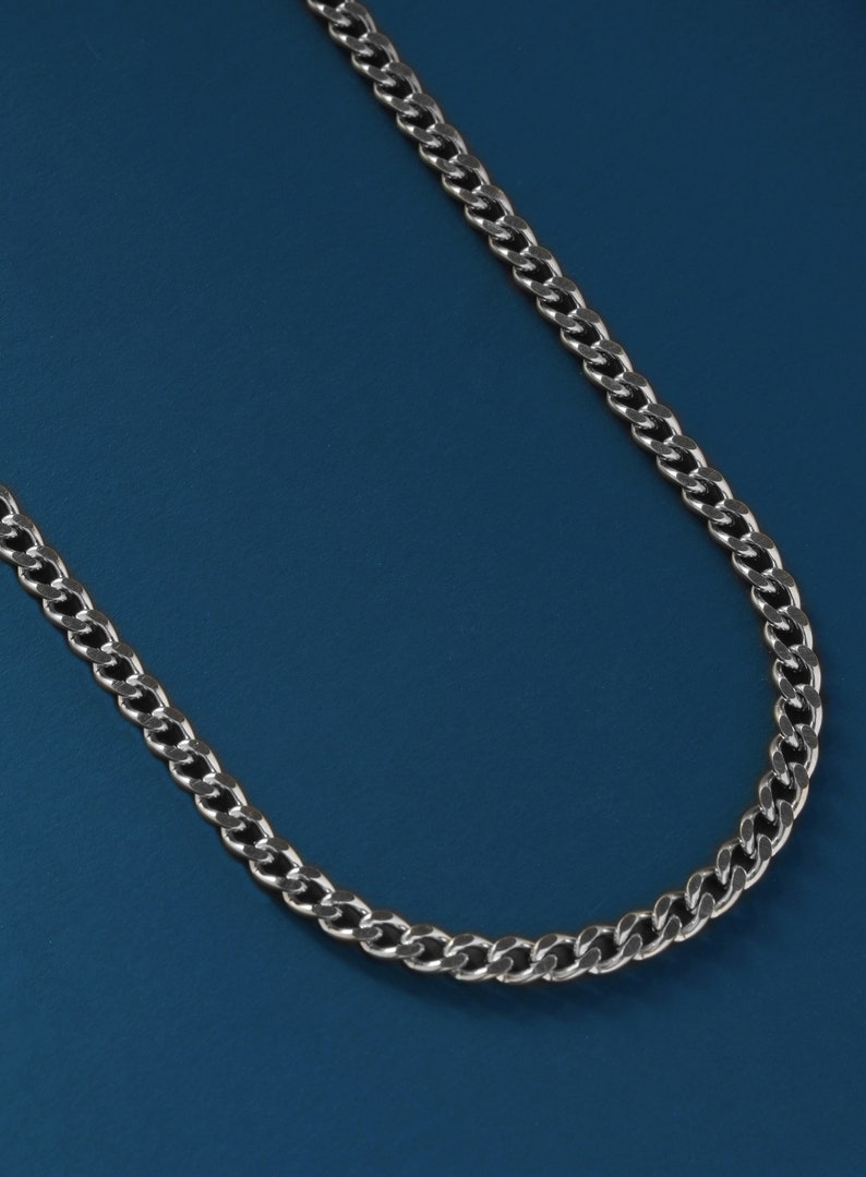 May include: A silver chain necklace with a curb link design. The chain is on a blue background.