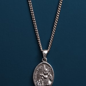 Pu&ograve; includere: Collana con catena d'argento con un ciondolo ovale d'argento con un designo di angelo custode. Il ciondolo ha le parole "Guardian Angel" incise su di esso.