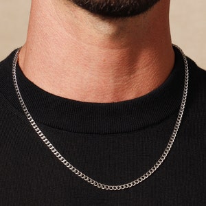 May include: A silver chain necklace worn on a person wearing a black shirt.
