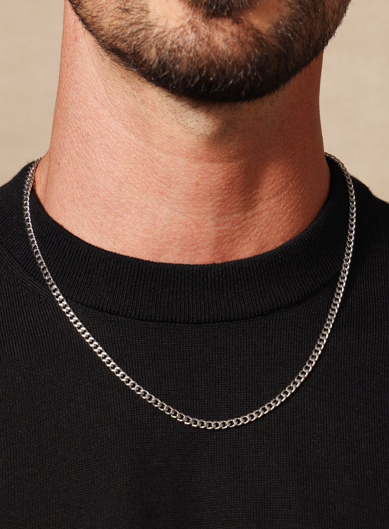 May include: A silver chain necklace worn on a person wearing a black shirt.