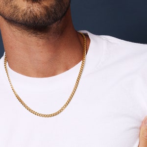 May include: A gold chain necklace on a person wearing a white t-shirt.