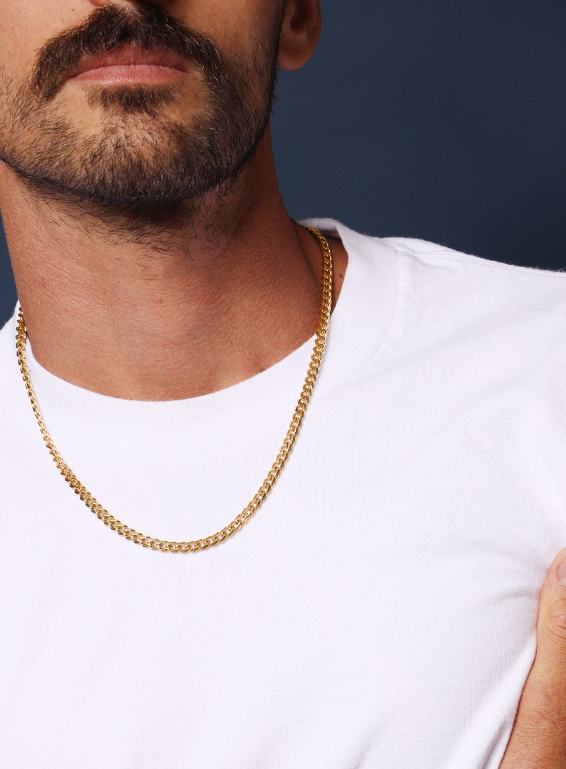 May include: A gold chain necklace on a person wearing a white t-shirt.