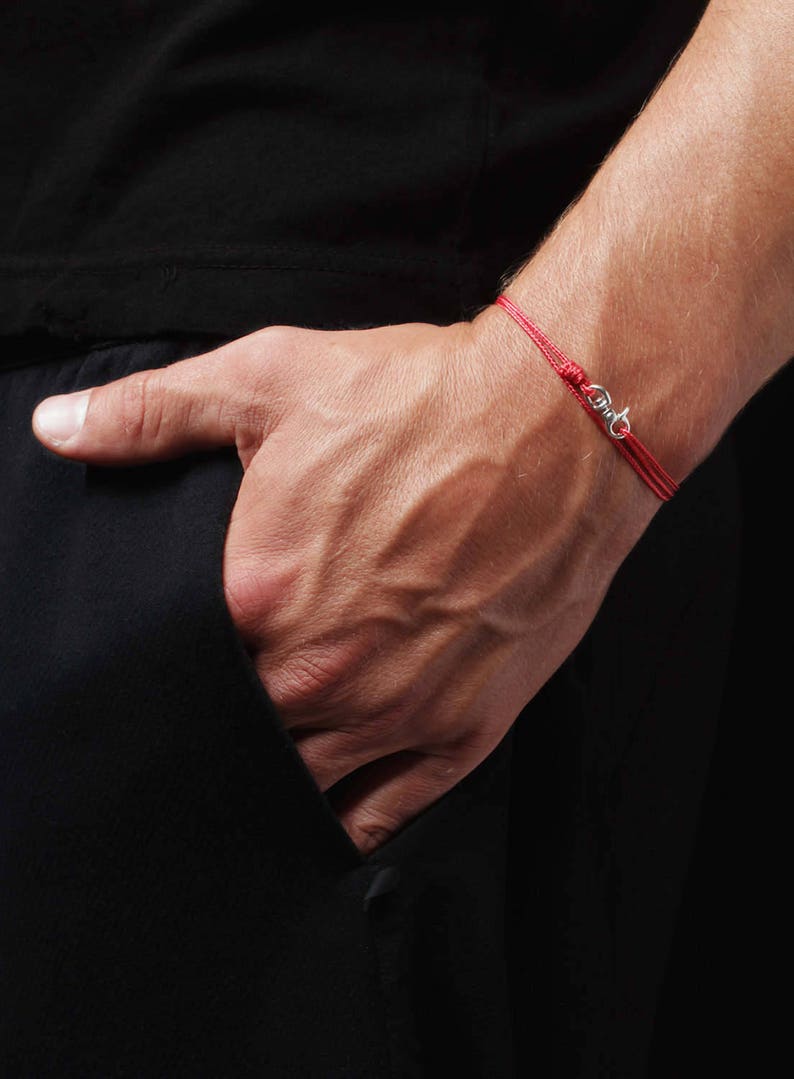May include: A red string bracelet with a silver clasp. The bracelet is worn on a person's wrist.