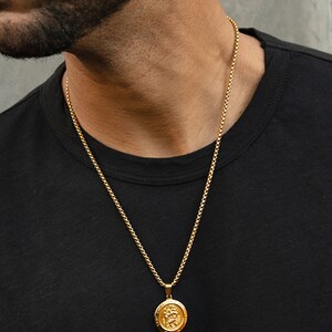 May include: A gold chain necklace with a round pendant featuring a detailed design. The pendant is hanging from a thin gold chain.