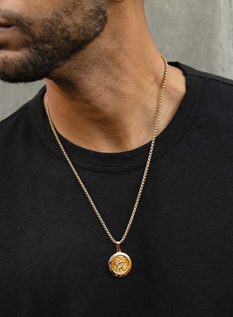 May include: A gold chain necklace with a round pendant featuring a detailed design. The pendant is hanging from a thin gold chain.