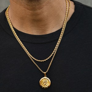 May include: A gold chain necklace with a gold pendant featuring a Saint Christopher medal. The pendant has the words "Saint Christopher Protect Us" inscribed around the edge.