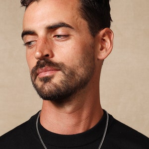 May include: A man wearing a black shirt with a silver chain necklace.