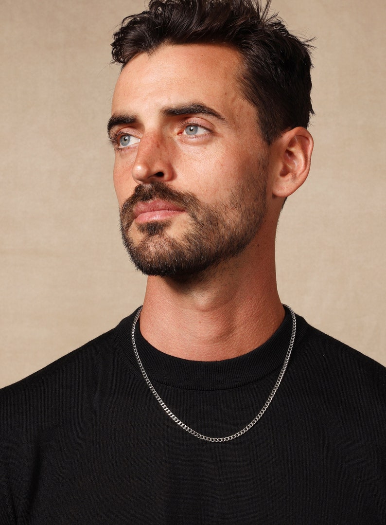 May include: A man wearing a black shirt with a silver chain necklace.