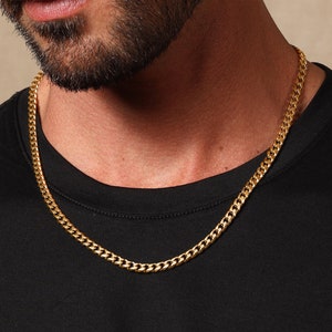 May include: A gold chain necklace with a curb link style. The chain is worn by a person with a beard.
