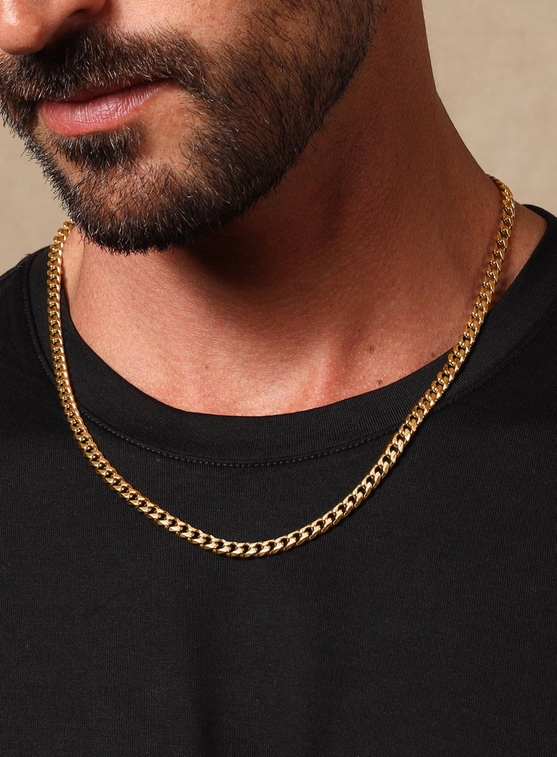 May include: A gold chain necklace with a curb link style. The chain is worn by a person with a beard.