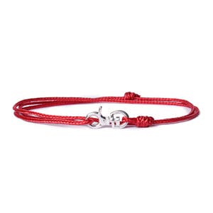 May include: A red cord bracelet with a silver clasp. The bracelet is made of a thin, braided cord and has a simple, elegant design.