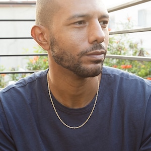 May include: A man wearing a dark blue t-shirt with a gold rope chain necklace.
