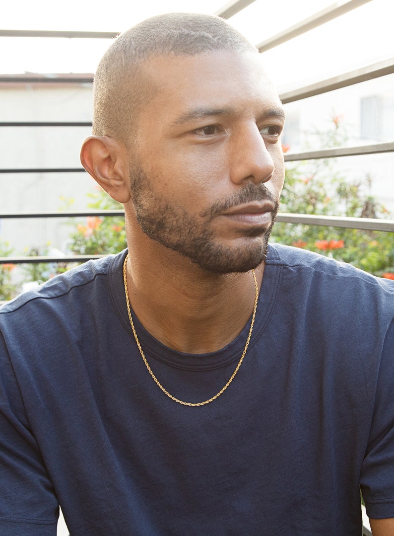 May include: A man wearing a dark blue t-shirt with a gold rope chain necklace.