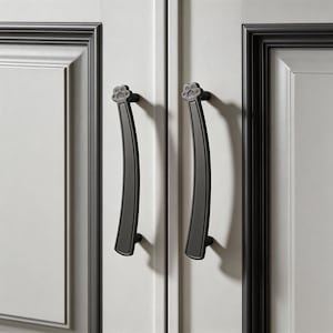 Puede incluir: Dos tiradores de armario negros con un diseño de huella de pata en la parte superior. Los tiradores son curvos y están montados en una puerta de armario blanca. La puerta del armario tiene un borde gris oscuro.