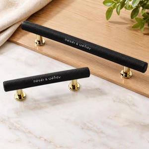 Puede incluir: Dos tiradores de armario cilíndricos con un acabado negro texturizado y soportes de montaje de metal dorado. Cada mango está grabado con el texto blanco Peter & Wendy. Los herrajes están diseñados para fijarse a muebles o puertas.