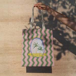 Peut inclure: Un sac fourre-tout avec un motif en zigzag vertical rose et vert. Le centre présente un graphique ovale contenant deux palmiers et le texte jaune HOSSEGOR. Le sac possède deux anses en tissu blanc cassé fixées au bord supérieur du corps rectangulaire.
