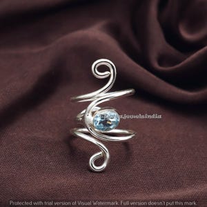 Könnte beinhalten: Ein silberfarbener Ring mit einem wirbelnden Design, der einen hellblauen, ovalen Edelstein in der Mitte aufweist. Das Design des Rings beinhaltet ein Spiralelement. Der Hintergrund ist ein dunkelbrauner Stoff.