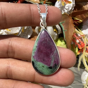 May include: A teardrop-shaped pendant featuring a polished ruby and zoisite stone with deep magenta and forest green color variations, set in a smooth silver bezel frame and suspended from a delicate silver chain link necklace.