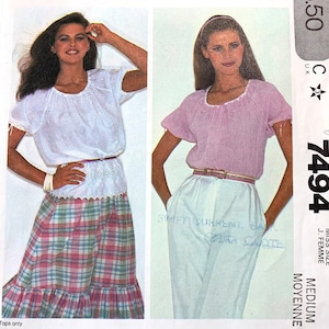 May include: A sewing pattern for two tops. The pattern is for a medium size and is called "7494". The tops are both white with a ruffled neckline and short sleeves. One top is white and the other is pink.
