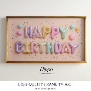 以下が含まれることがあります： カラフルな風船の文字で「HAPPY BIRTHDAY」と書かれた額装されたアートワーク。風船は紫、黄色、ピンク、青の色合いで、紙吹雪と小さな風船のあるピンク色の背景に配置されています。フレームは金色です。