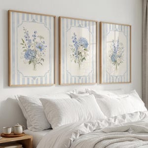 May include: Three framed wall art prints featuring watercolour-style floral bouquets in shades of blue and white. Each print is centred within a decorative border against a background of vertical light blue and white stripes in wooden frames.