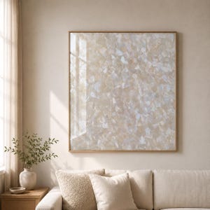 May include: A square wall art piece featuring a mosaic of iridescent, off-white, and cream-colored shell fragments arranged in a dense, overlapping pattern. The artwork is encased in a thin, light-toned wooden frame with a smooth, reflective surface.