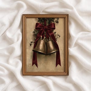 Può includere: Una stampa artistica incorniciata raffigurante due campane metalliche color ottone appese a un fiocco di velluto rosso scuro. Le campane sono posizionate sopra un grappolo di fogliame verde su uno sfondo beige chiaro testurizzato in una cornice dorata.