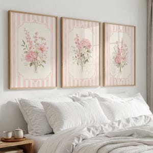 May include: Three framed wall art prints featuring floral bouquets in shades of pink and white. Each print is set against a background of vertical light pink and white stripes, enclosed within a decorative border, displayed in light wood frames.