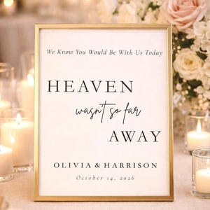 May include: A framed sign with gold trim displays the text "We Know You Would Be With Us Today," followed by "HEAVEN wasn't so far AWAY." The sign is for Olivia & Harrison, dated October 14, 2026. The background includes candles and flowers.