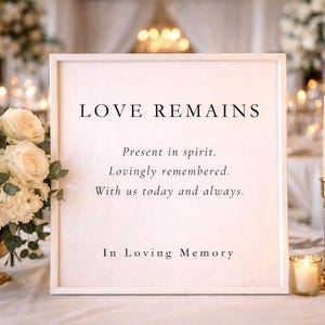May include: A white framed sign with black text reading LOVE REMAINS, Present in spirit. Lovingly remembered. With us today and always. In Loving Memory. The sign is flanked by a bouquet of white roses and a tall taper candle in a gold holder.